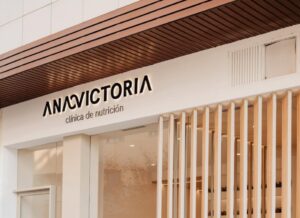 Fotografía del logotipo ANAVICTORIA en la fachada de su clínica de nutrición, en un entorno moderno con acabados en madera y tonos neutros.